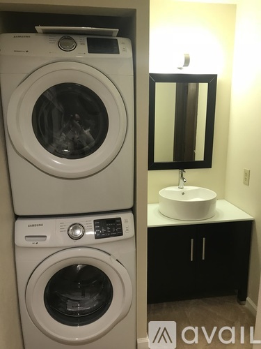 A stacked white washer and dryer in a small bathroom with a white sink and black cabinet.