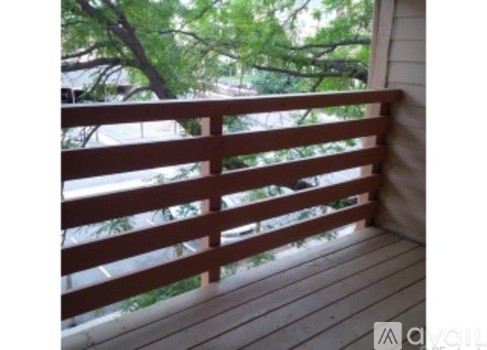 A wooden balcony with a railing and a view of trees and a building in the background.