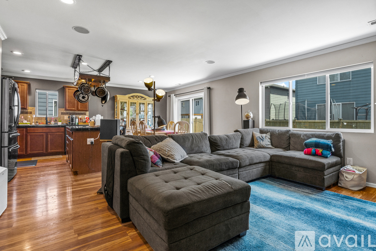 A modern living room with a grey sectional sofa and a kitchen area with wooden cabinets.