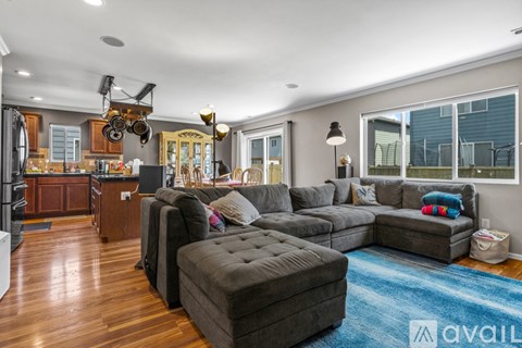 A modern living room with a grey sectional sofa and a kitchen area with wooden cabinets.