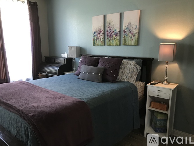 A bedroom with a bed, nightstand, and a painting on the wall.