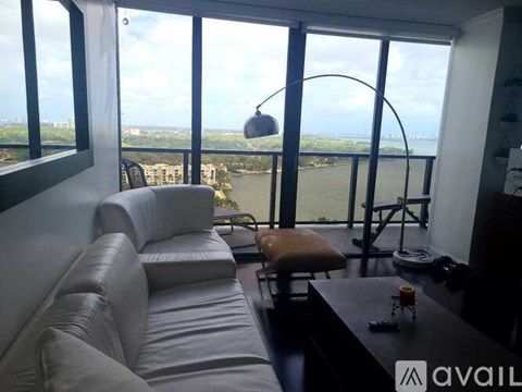 A living room with a white couch and a large window overlooking a body of water.