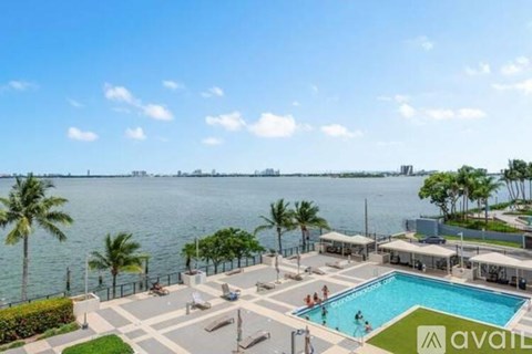 A pool area with a view of the water and palm trees.