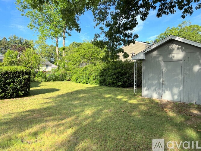 A shed sits in a grassy yard with trees in the background.