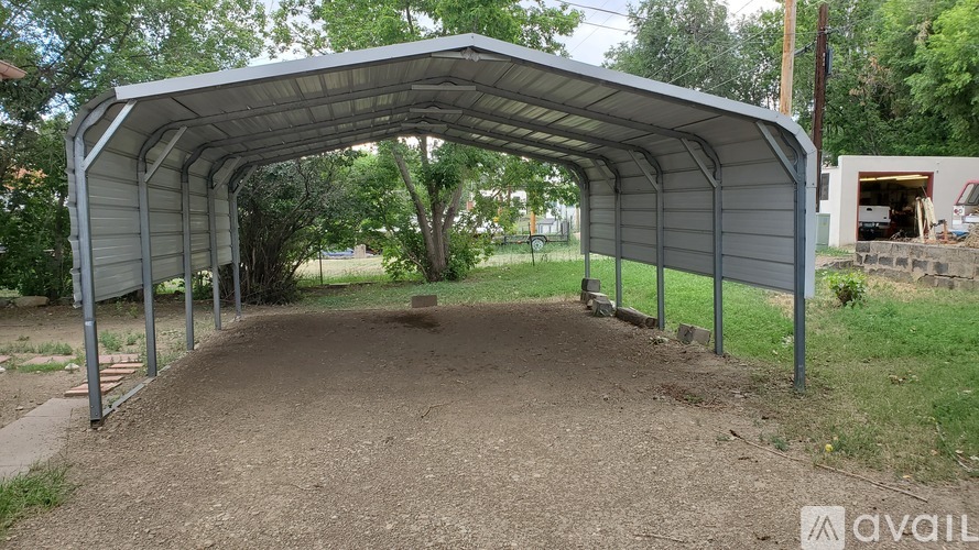 A large metal structure with a curved roof is situated in a grassy area with a dirt path leading up to it.