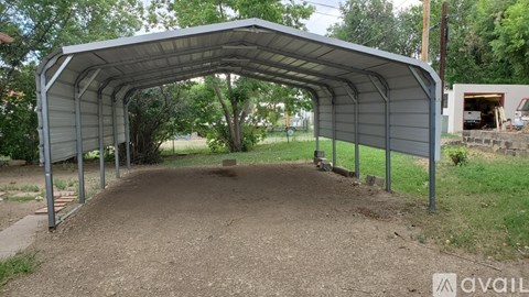 A large metal structure with a curved roof is situated in a grassy area with a dirt path leading up to it.