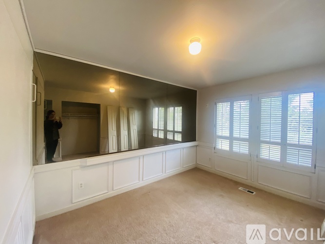 A spacious room with a large mirror and a window with white blinds.