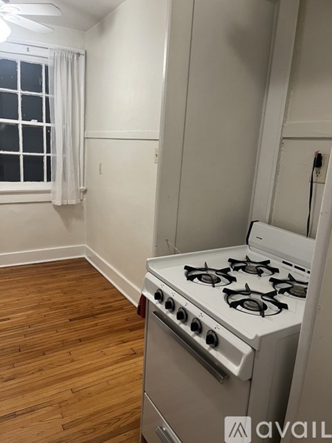 A white gas stove in a kitchen with wooden flooring and a window with white curtains.