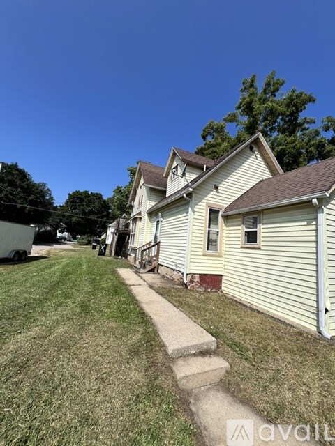 A house with a white siding and a brown roof is shown with a clear blue sky in the background.