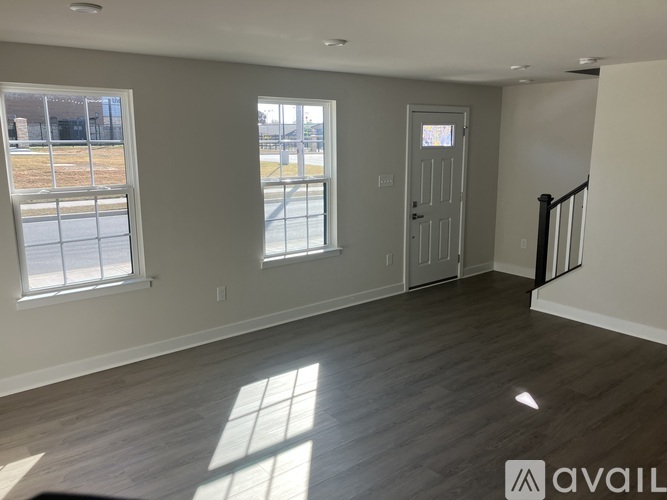 A spacious room with wooden flooring and a staircase on the right.