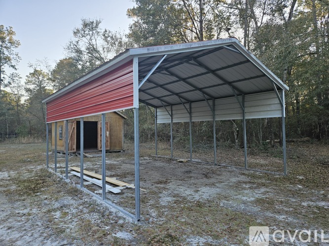 A metal carport with a red roof is in a field.