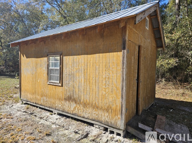 A small wooden shed with a metal roof and a door is situated in a grassy area.