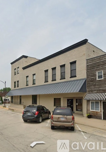 A building with a black awning and two cars parked in front.