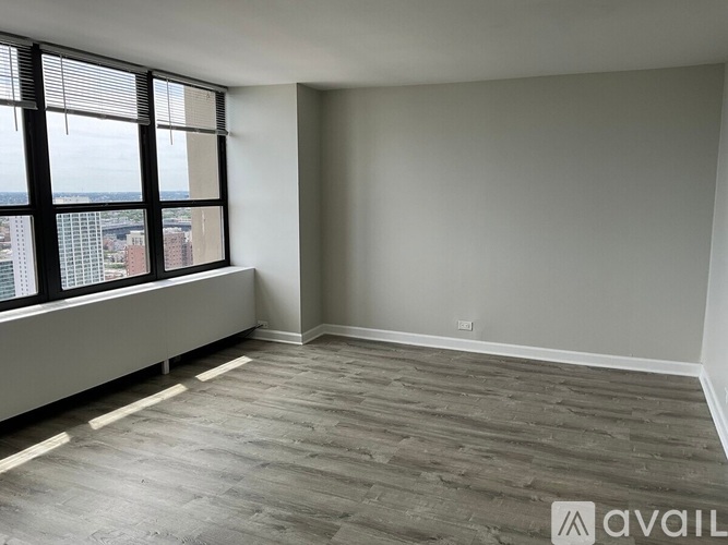 A room with a large window and wooden flooring is available for rent.