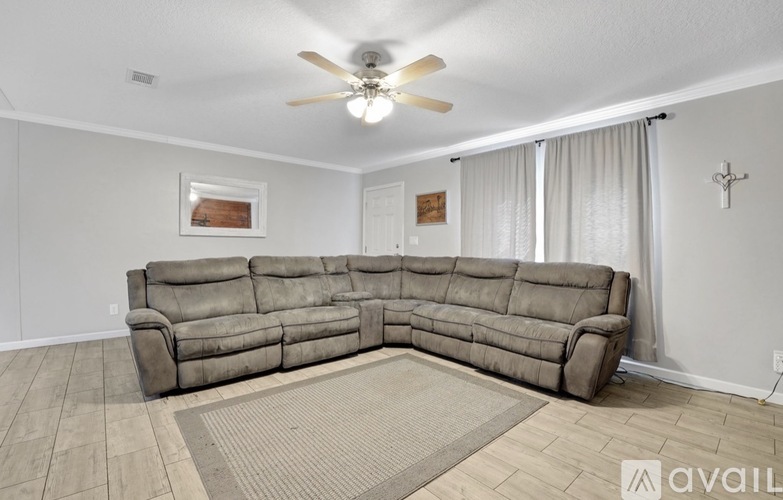 A large grey sectional sofa sits in a spacious living room with a rug on the floor and a ceiling fan above.