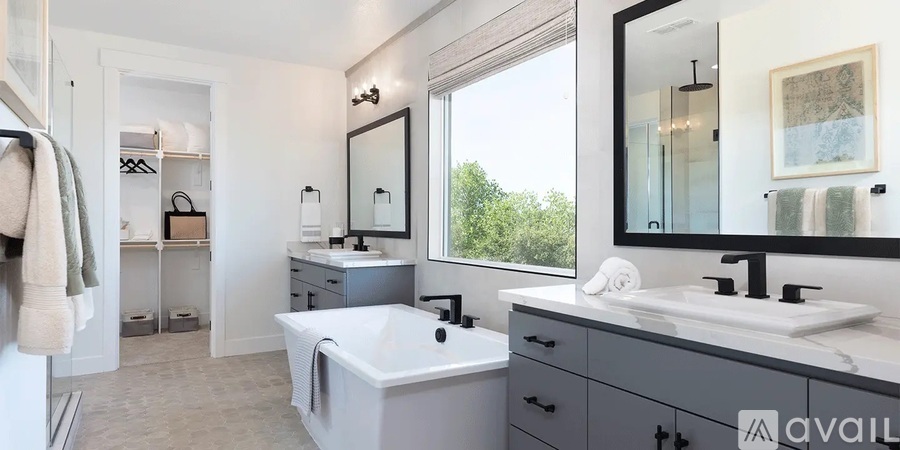 A bathroom with a white tub and sink, a large mirror, and a window with a view of trees.