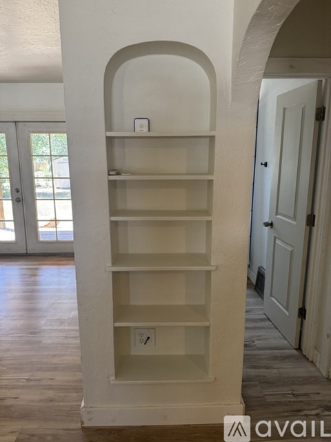 A white shelving unit with glass doors is in a room with a door and a window.
