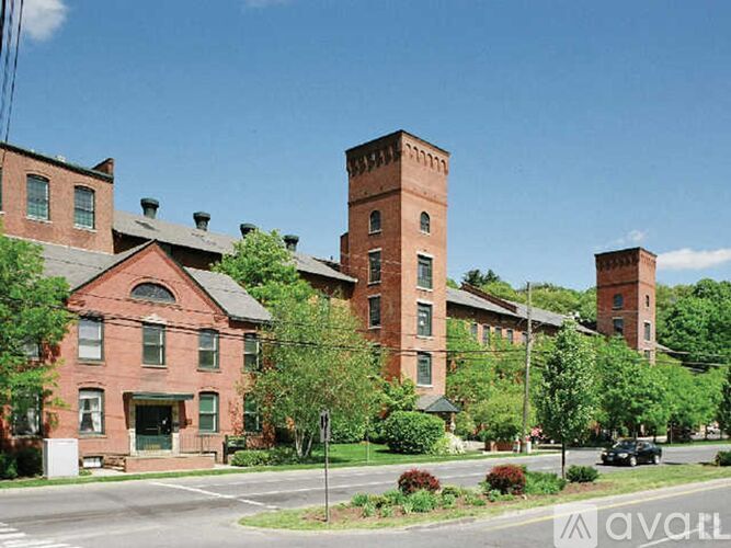 A large red brick building with a tower is surrounded by green trees.