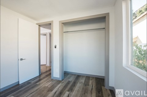 A room with a white door, a white wall, and a window with a view of trees outside.