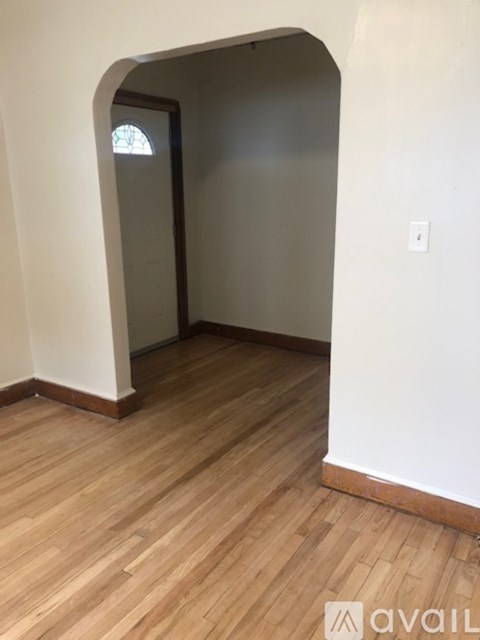 A room with wooden flooring and a white wall with a window.