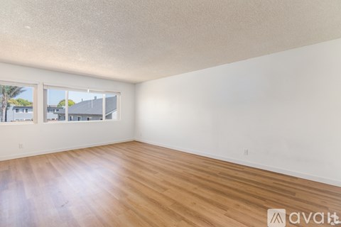 A room with wooden flooring and white walls, with a window showing a view of buildings outside.