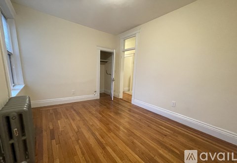A room with wooden floors and white walls, with a doorway leading to another room.