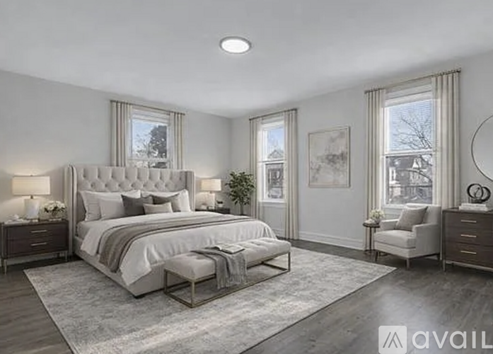 A well-lit bedroom with a large bed, a side table with a lamp, and a chair.