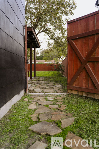 A wooden gate leads to a backyard with a stone path.