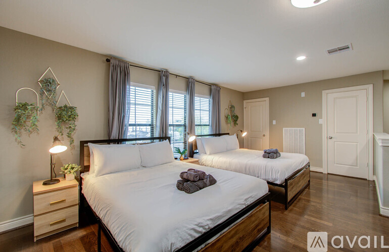 A bedroom with two beds, one with a white comforter and the other with a white sheet, and a nightstand with a lamp.