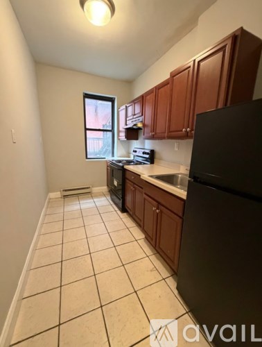 A kitchen with a black refrigerator, white tiled floor, and brown cabinets.