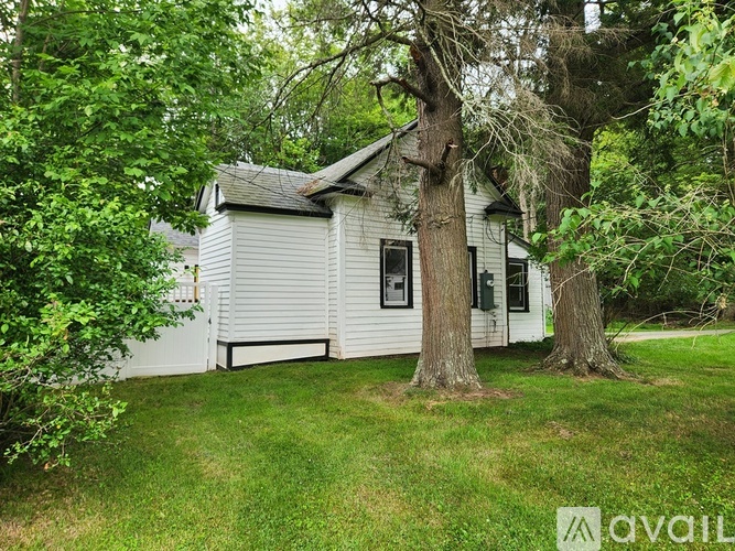 A small white house with a black roof is surrounded by trees.