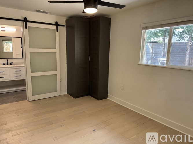 A room with a wooden floor, a ceiling fan, and a window with a view of trees outside.