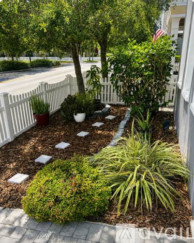 A garden with a white picket fence and a variety of plants.