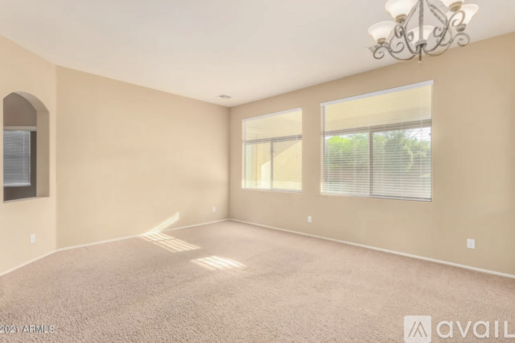 A large empty room with a chandelier and a window with blinds.