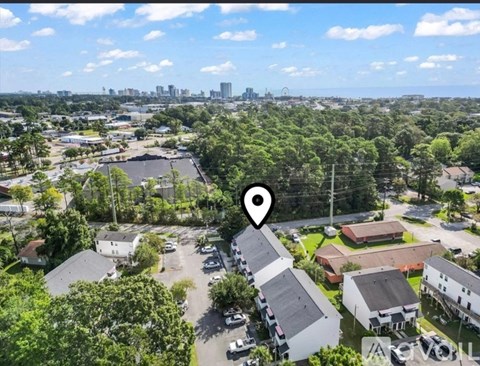 A bird's eye view of a residential area with a large green space in the foreground and a city skyline in the distance.