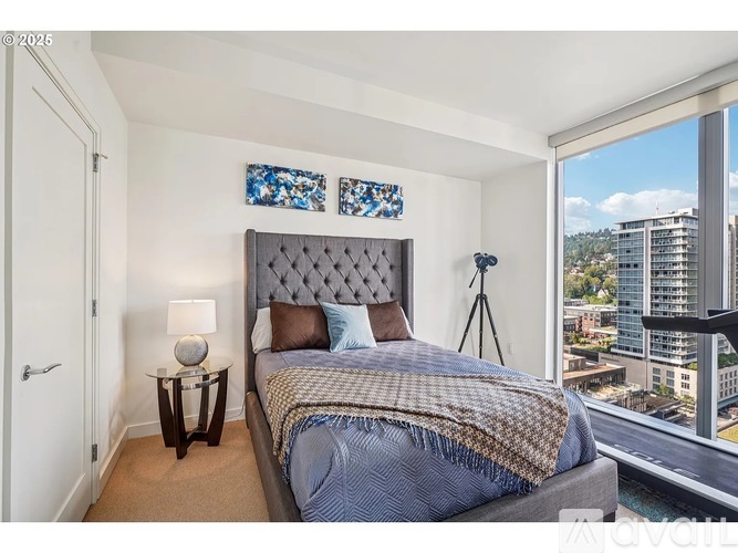 A bedroom with a large bed and a city view through the window.