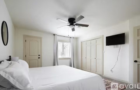 A bedroom with a bed, a ceiling fan, and a window with curtains.