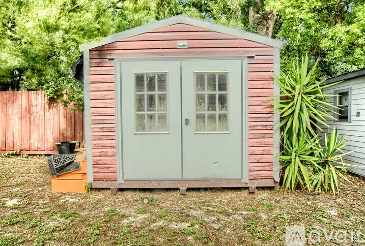 A small wooden shed with a grey door stands in a grassy area.