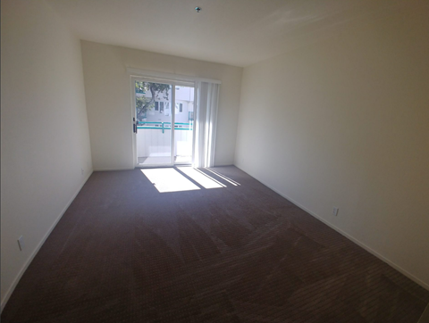 A room with a brown floor and a door leading outside.
