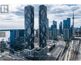 Two tall buildings are in the foreground of a cityscape with a highway and other buildings in the background.