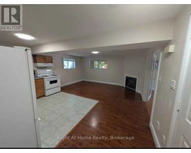 A spacious room with wood flooring and a white refrigerator.