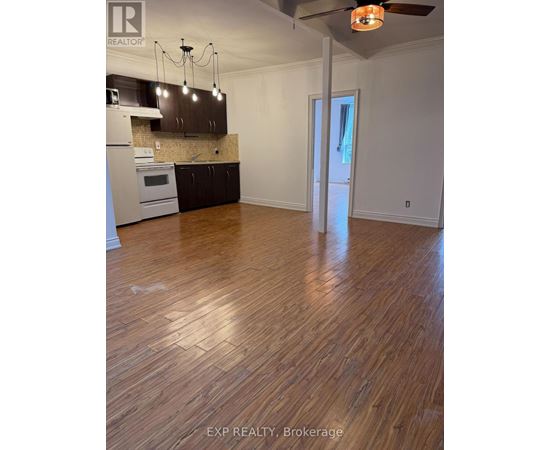 A room with wooden floors and a kitchen area with a stove and cabinets.