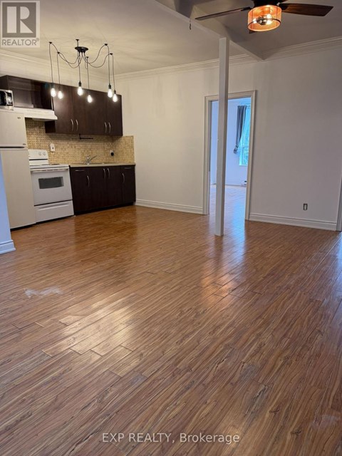 A room with wooden floors and a kitchen area with a stove and cabinets.