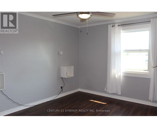 A room with a ceiling fan and a window with white curtains.