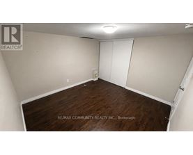 A room with a wooden floor and white walls, with a sign that reads "RE/MAX COMMUNITY REALTY INC., Brokerage".