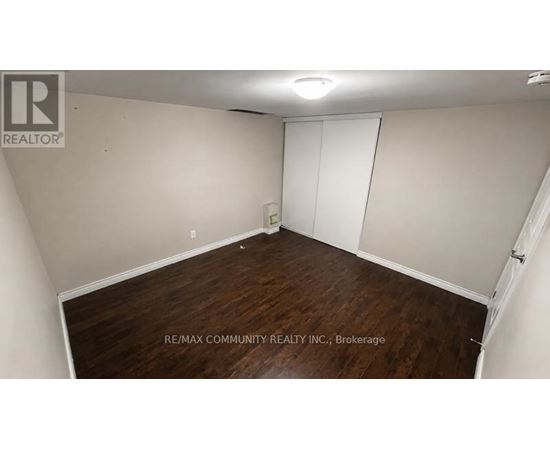 A room with a wooden floor and white walls, with a sign that reads "RE/MAX COMMUNITY REALTY INC., Brokerage".
