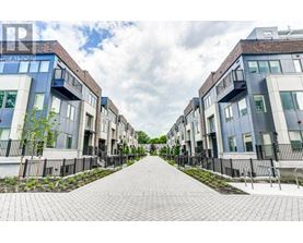 A row of modern townhouses with a paved walkway in the foreground.