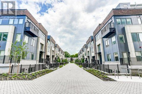 A row of modern townhouses with a paved walkway in the foreground.