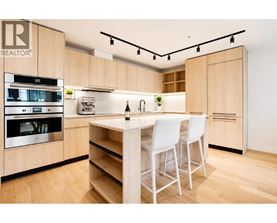 A modern kitchen with wooden cabinets and white chairs.
