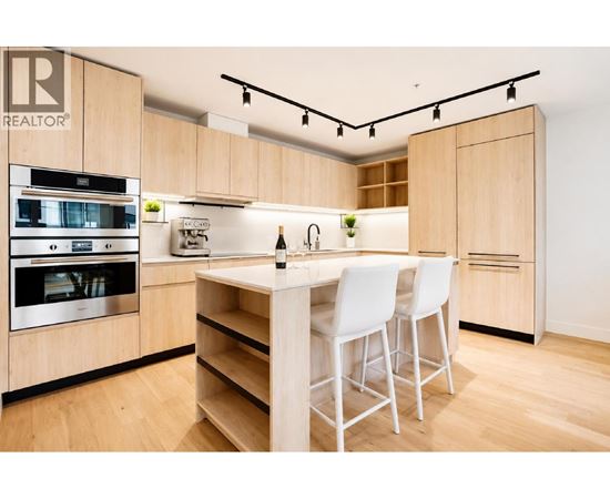 A modern kitchen with wooden cabinets and white chairs.
